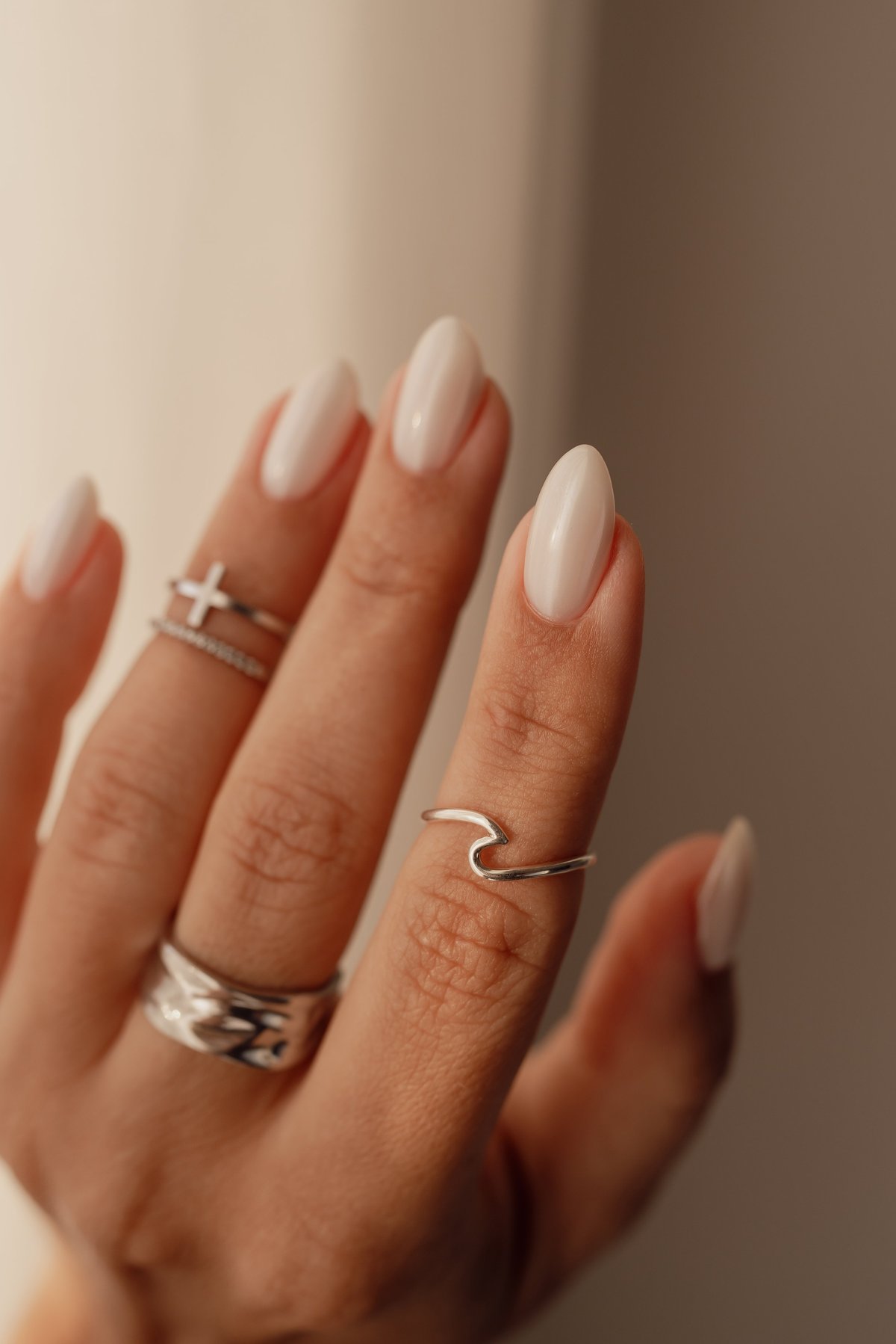 Vertical shot of a young woman's hand with almond-shaped chrome gel nails and stylish silver rings, softly lit by daylight